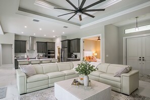 A modern living room with a sectional sofa, a coffee table, and a ceiling fan. - Brand-new Luxury Home w/ Pool! 9 Mi to Pine Island (Cape Coral)