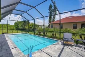 A covered outdoor swimming pool with a clear view of a house and surrounding greenery. - Brand-new Luxury Home w/ Pool! 9 Mi to Pine Island (Cape Coral)