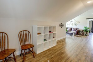 Une pièce avec une étagère blanche, deux chaises en bois, un canapé en cuir marron et une plante en pot.