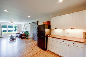 A spacious kitchen with wooden flooring, white cabinets, and a black refrigerator.