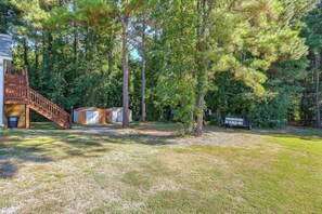 A residential property with a wooden staircase leading to a deck, a small shed, and a fenced area with trees.