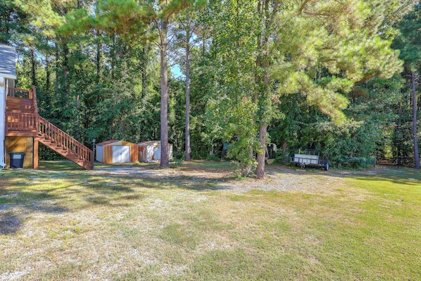 A residential property with a wooden staircase leading to a deck, a small shed, and a fenced area with trees.