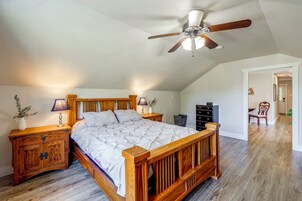 Quarto com cama de madeira, duas mesas de cabeceira, ventilador de teto e mesa de apoio com abajur.