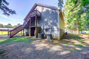 A building with a wooden staircase leading to a balcony, outdoor air conditioning unit, and a gravel driveway.