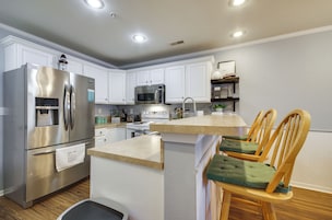 Una cocina moderna con electrodomésticos de acero inoxidable, muebles de cocina blancos y una isla central con sillas acolchadas color verde.
