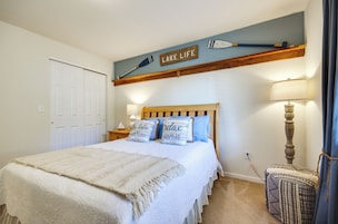 Un dormitorio con una cama, una mesita de noche, una lámpara, un estante en la pared con una paleta, y una puerta.