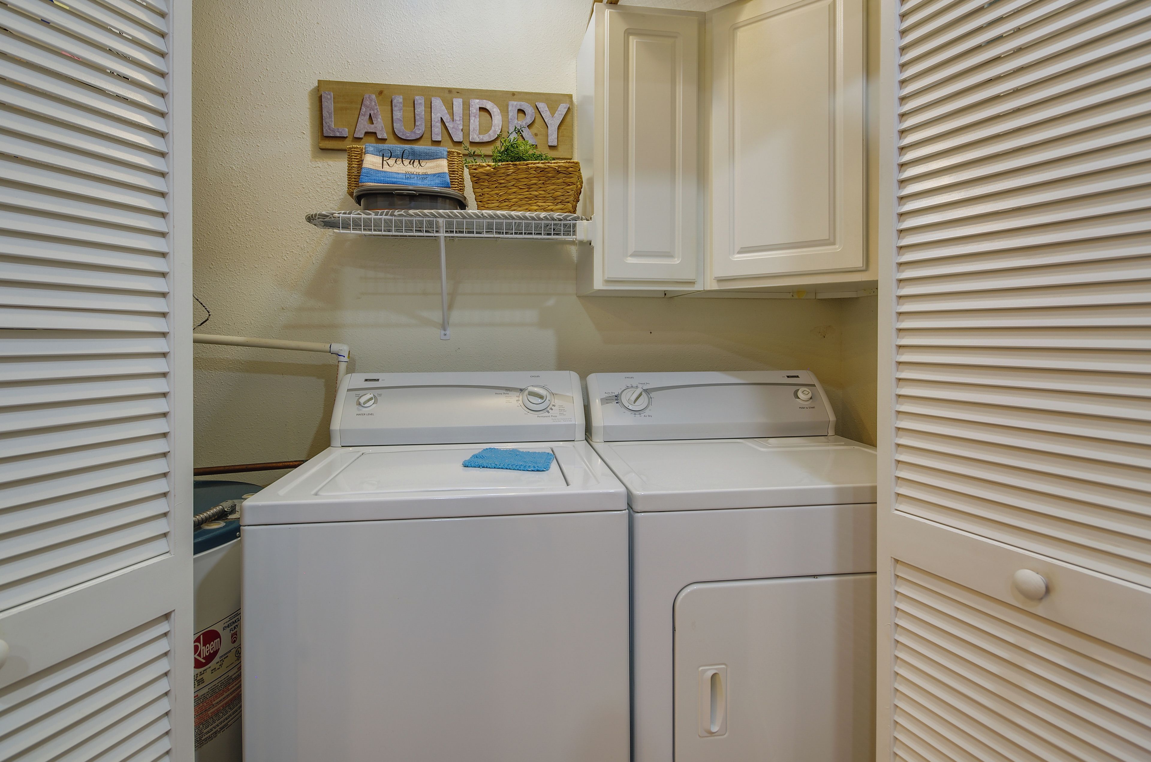 A laundry room with two front-loading washing machines, a shelf with a 'Laundry' sign, and a basket with a towel.