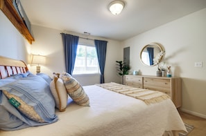 Een slaapkamer met een bed, een dressoir, een spiegel, een raam met gordijnen en een plafondlamp.