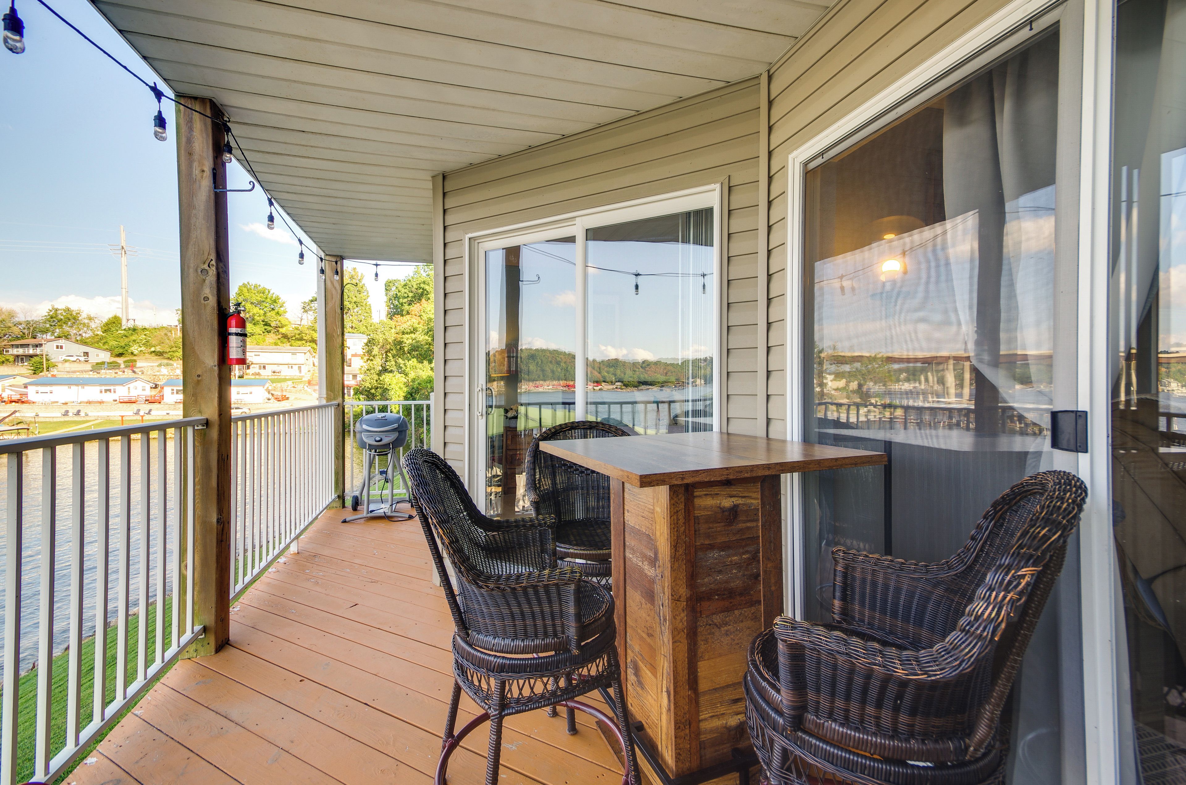 A covered outdoor deck with wicker furniture and a bar area, overlooking a body of water and a distant landscape.
