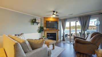 Una sala de estar con chimenea, ventilador de techo y vistas al exterior.