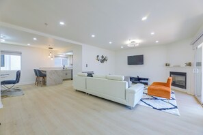 A modern living room with a white sofa, a TV mounted on the wall, and a fireplace. - Extended Stay Near Beaches & LA Commuter Routes (Torrance)