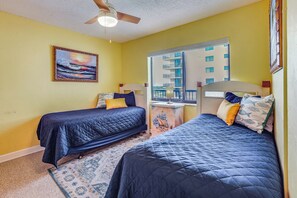 A room with two beds, a ceiling fan, a painting, and a window with a view of a building. - Oceanfront Paradise on No-drive New Smyrna Beach (New Smyrna Beach)