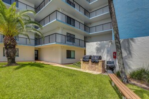 A multi-story residential building with balconies, a well-maintained lawn, and outdoor barbecue equipment. - Oceanfront Paradise on No-drive New Smyrna Beach (New Smyrna Beach)