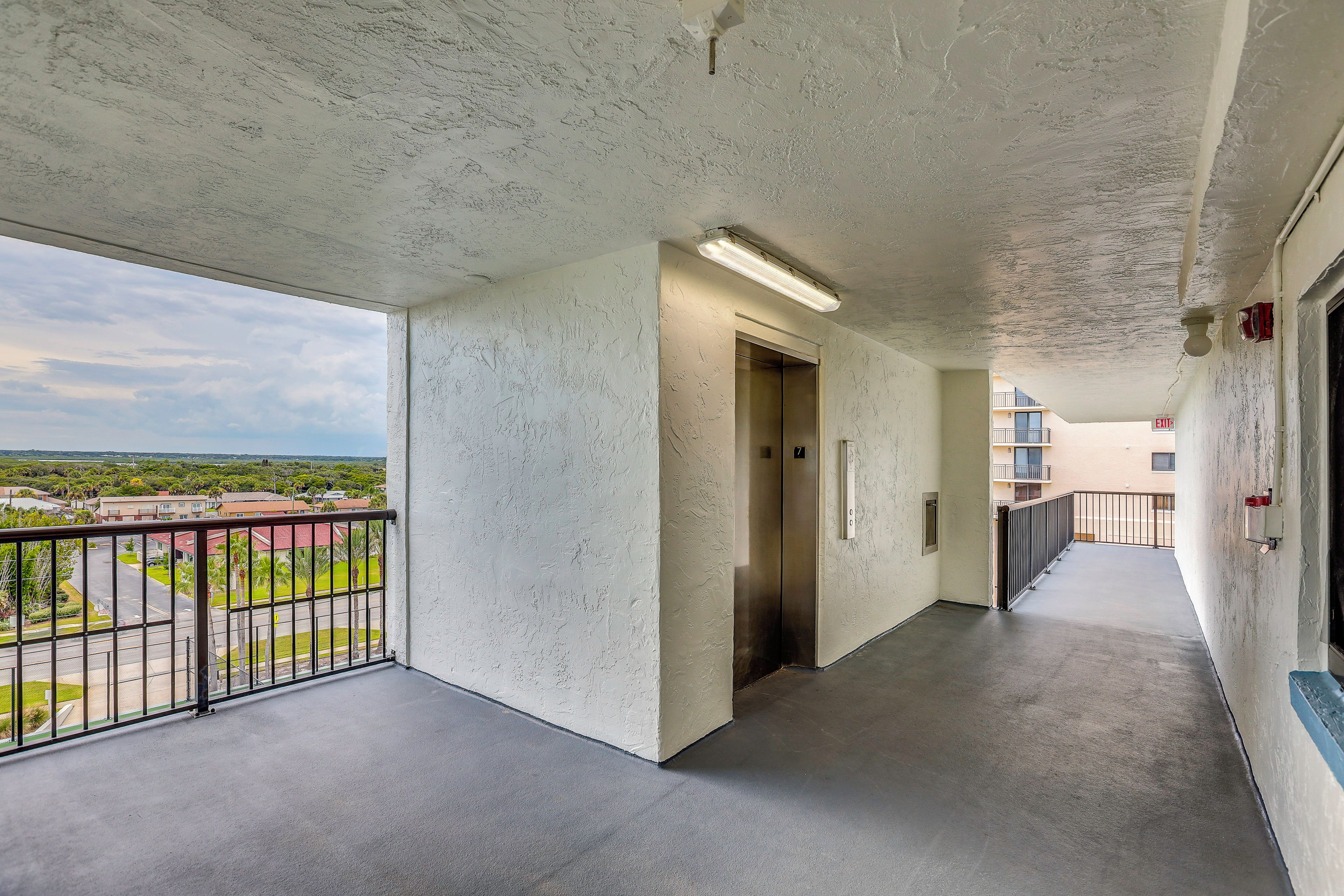 A corridor with a view of a residential area, a door, and an elevator.