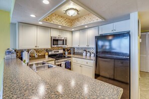 A kitchen with granite countertops, stainless steel appliances, and white cabinetry. - Oceanfront Paradise on No-drive New Smyrna Beach (New Smyrna Beach)
