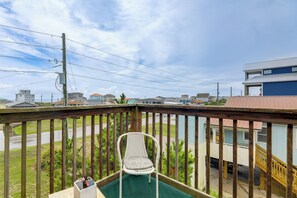 A balcony with a chair and a small table, overlooking a street with houses and a clear sky. - Walk to Ocean! Family Condo in North Topsail Beach (Sneads Ferry)