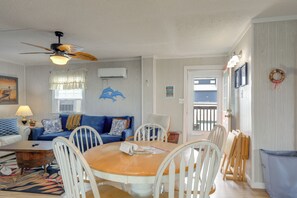 A dining area with a round table, white chairs, a ceiling fan, and a view of the outside. - Walk to Ocean! Family Condo in North Topsail Beach (Sneads Ferry)