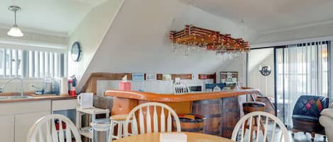 A kitchen with a wooden table, white chairs, a bar area, and a dining area with a view of the outside.