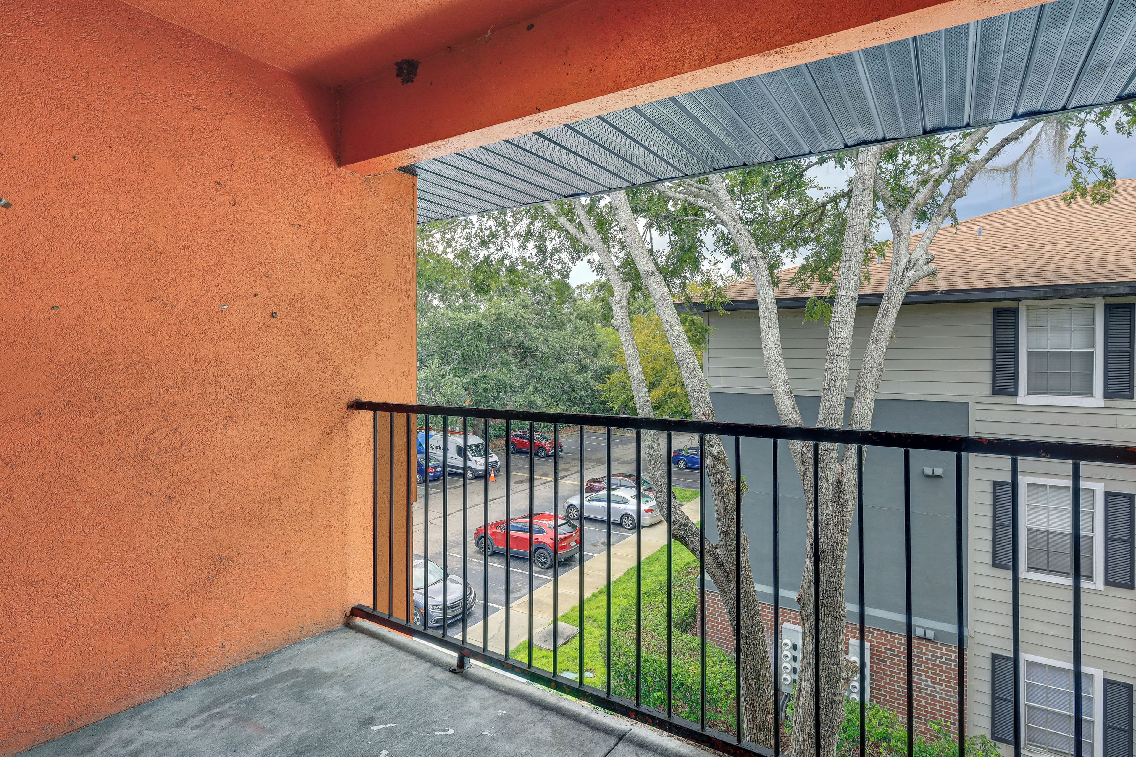 A balcony with a metal railing overlooking a parking area and a residential building.