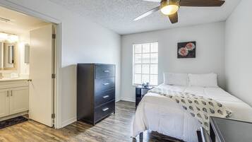 A bedroom with a bed, a dresser, a ceiling fan, a window with blinds, and a wall-mounted artwork.