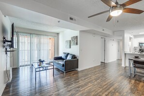Uma sala de estar espaçosa com ventilador de teto, sofá, mesa de centro e área de cozinha com micro-ondas.