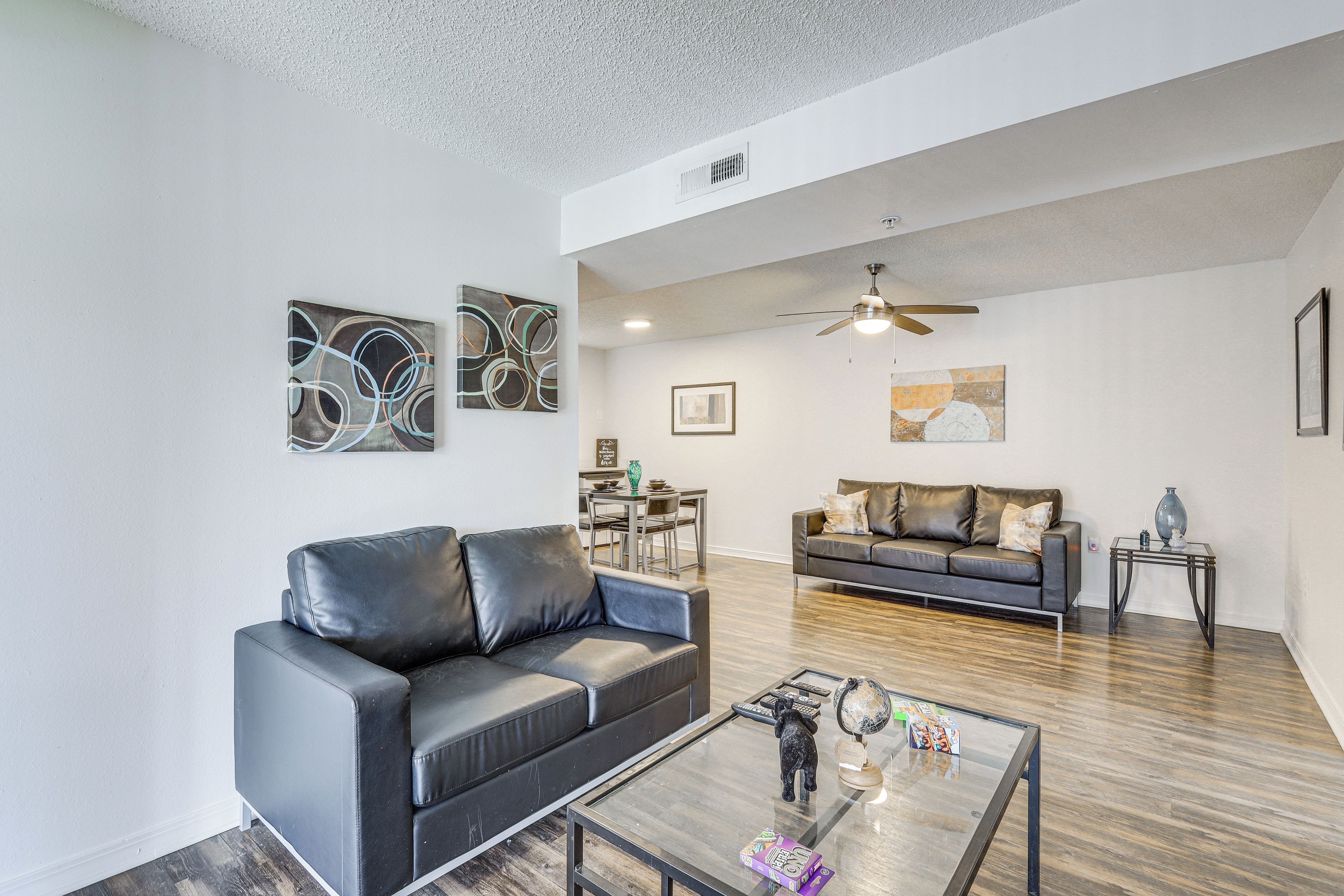 A modern living room with a black leather sofa, a glass coffee table, and abstract wall art.