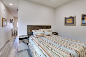 A bedroom with a wooden headboard, a striped bedspread, two pillows, a bedside table, and a nightstand. There are two framed artworks on the wall. - Trail Access & Views! 90-acre Haven in Hot Springs (Hot Springs)