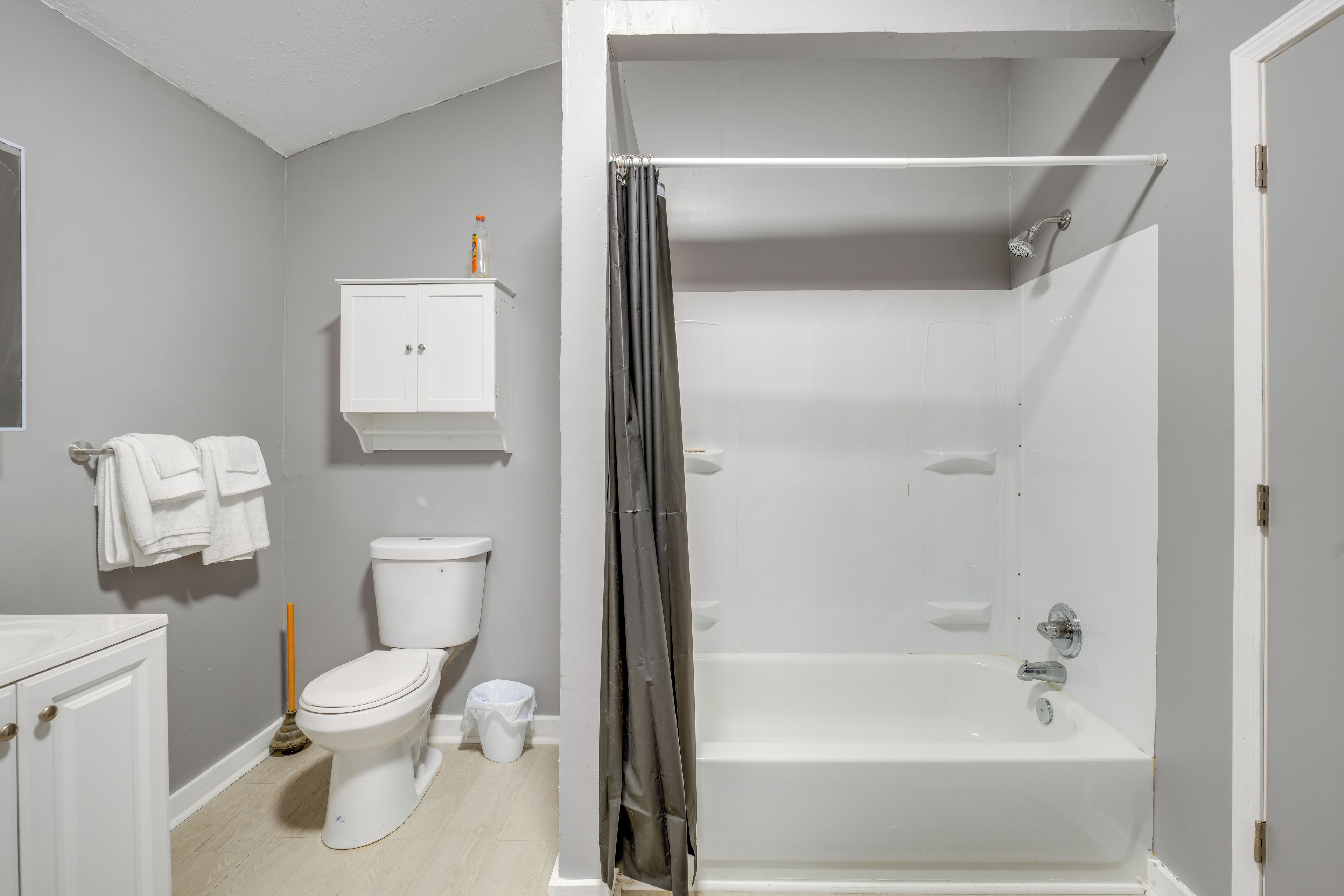 Et badeværelse med toilet, badekar, bruser og et skab.