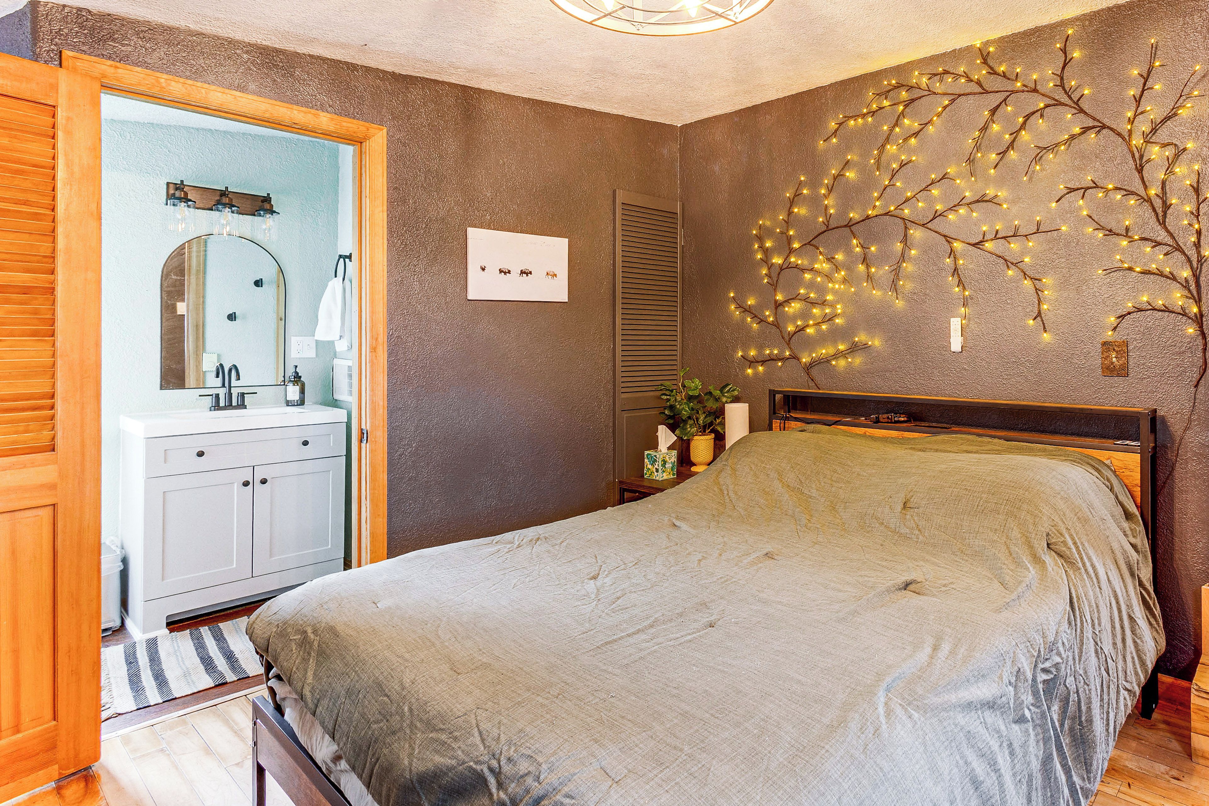 A bedroom with a bed, a bedside table, a mirror, a dresser, and a wall-mounted light fixture.