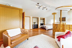 A spacious living area with a brown leather sofa, a white armchair, and a patterned rug. There is a wooden wardrobe, a dining table with chairs, and a bed in the background. - Deck & Views! Family Retreat Near Rmnp (Grand Lake)