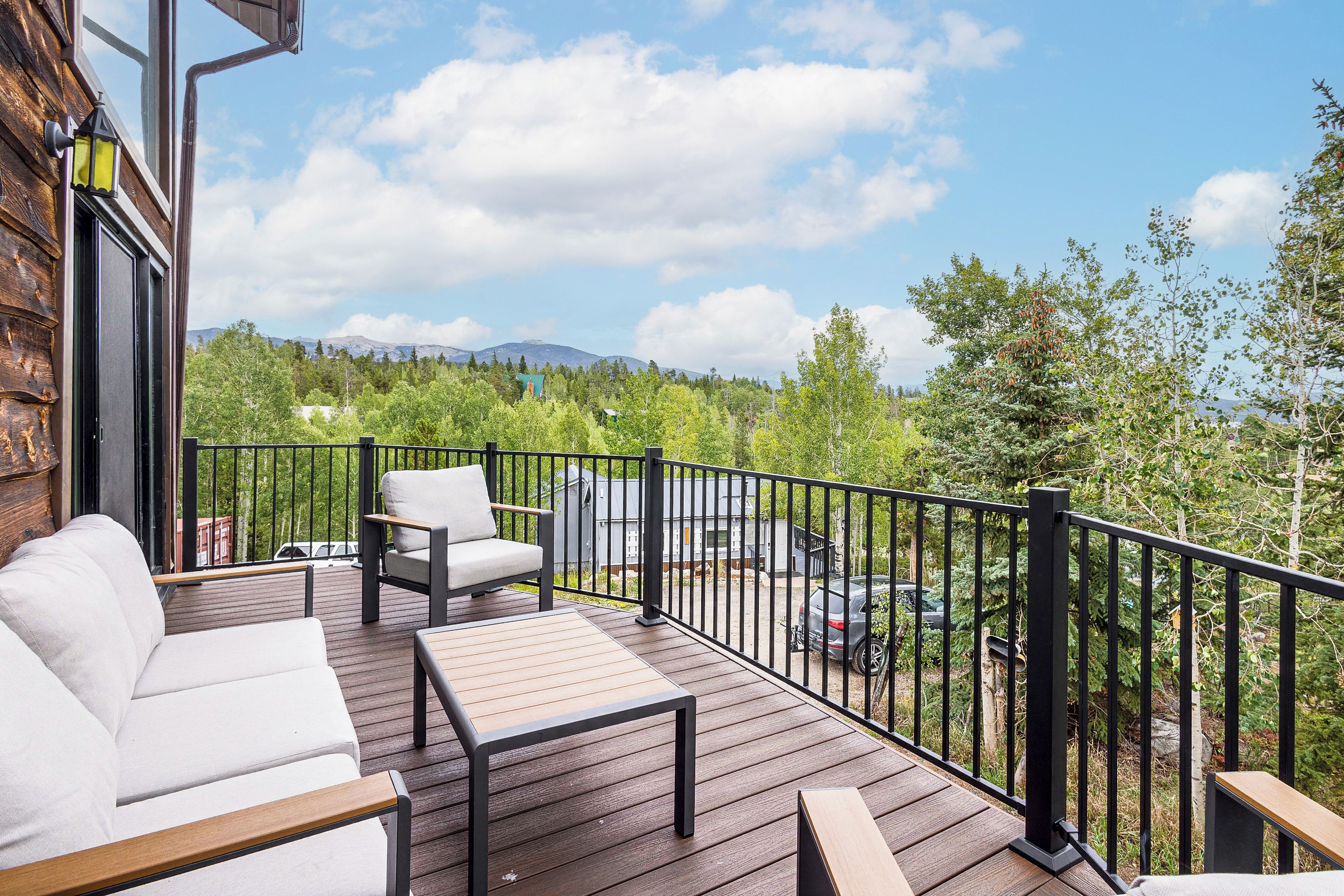 A deck with outdoor furniture, a view of a forest, and a mountain in the distance.