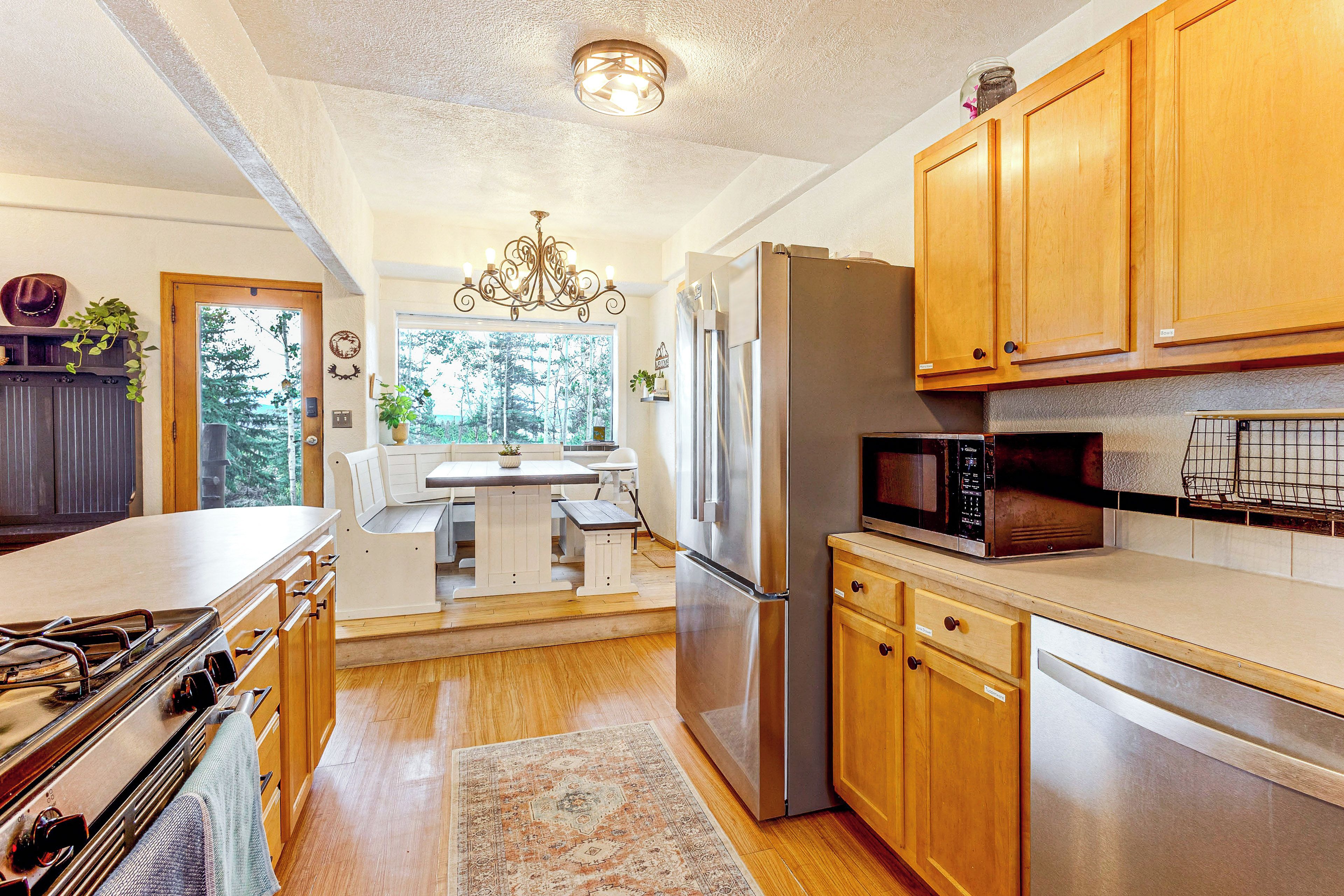 A kitchen with wooden cabinets, stainless steel appliances, a dining area with a table and chairs, and a view of trees through the window.
