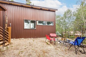 A brown metal building with two windows, a wooden deck, and two folding chairs.