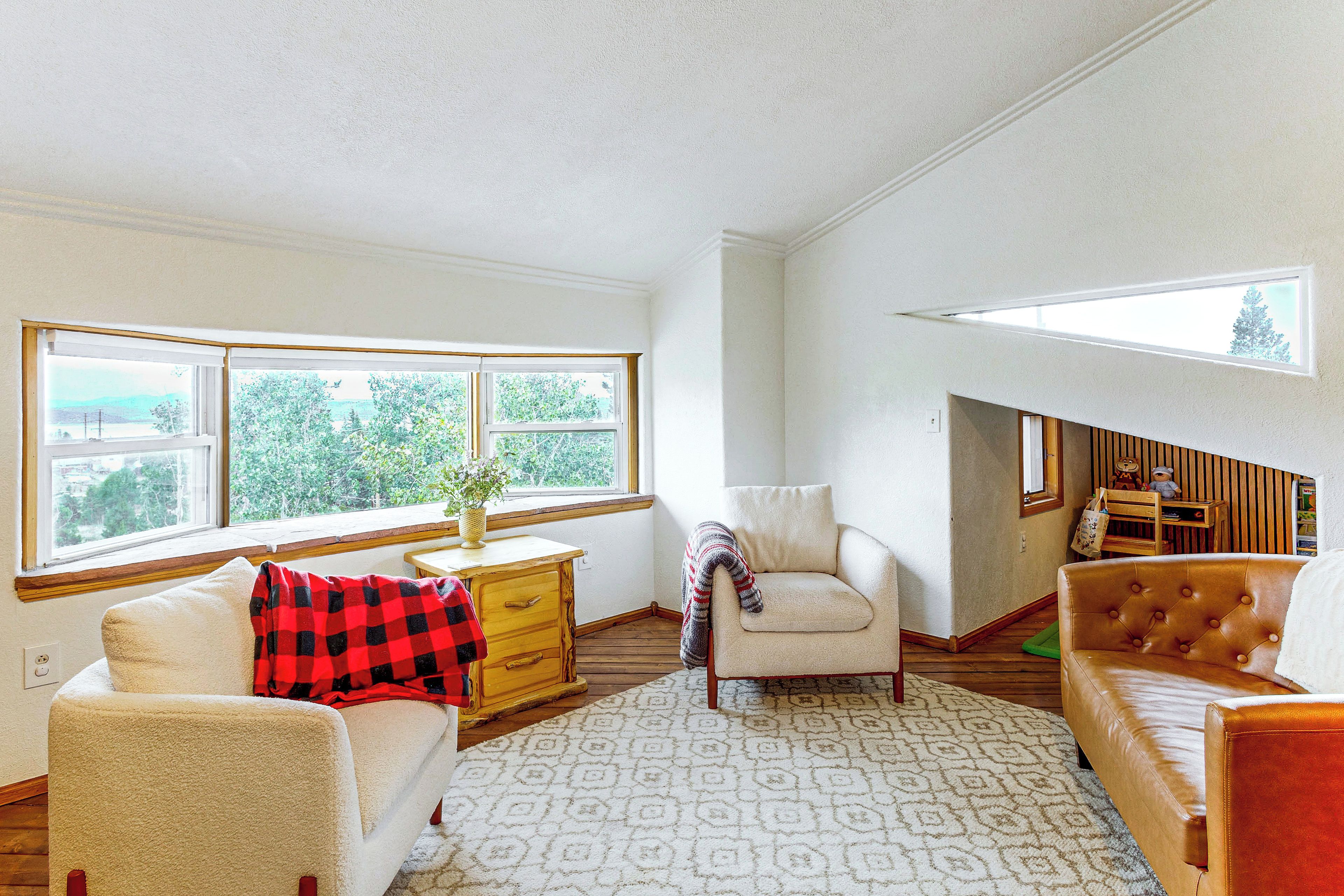 Una sala de estar con chimenea, un sofá, una silla y vistas al exterior a través de amplias ventanas.