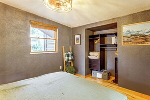 A bedroom with a bed, a window, a closet, and a painting on the wall.