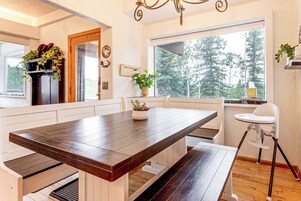 A modern kitchen with a wooden table, white cabinetry, and a large window offering a view of the outdoors.