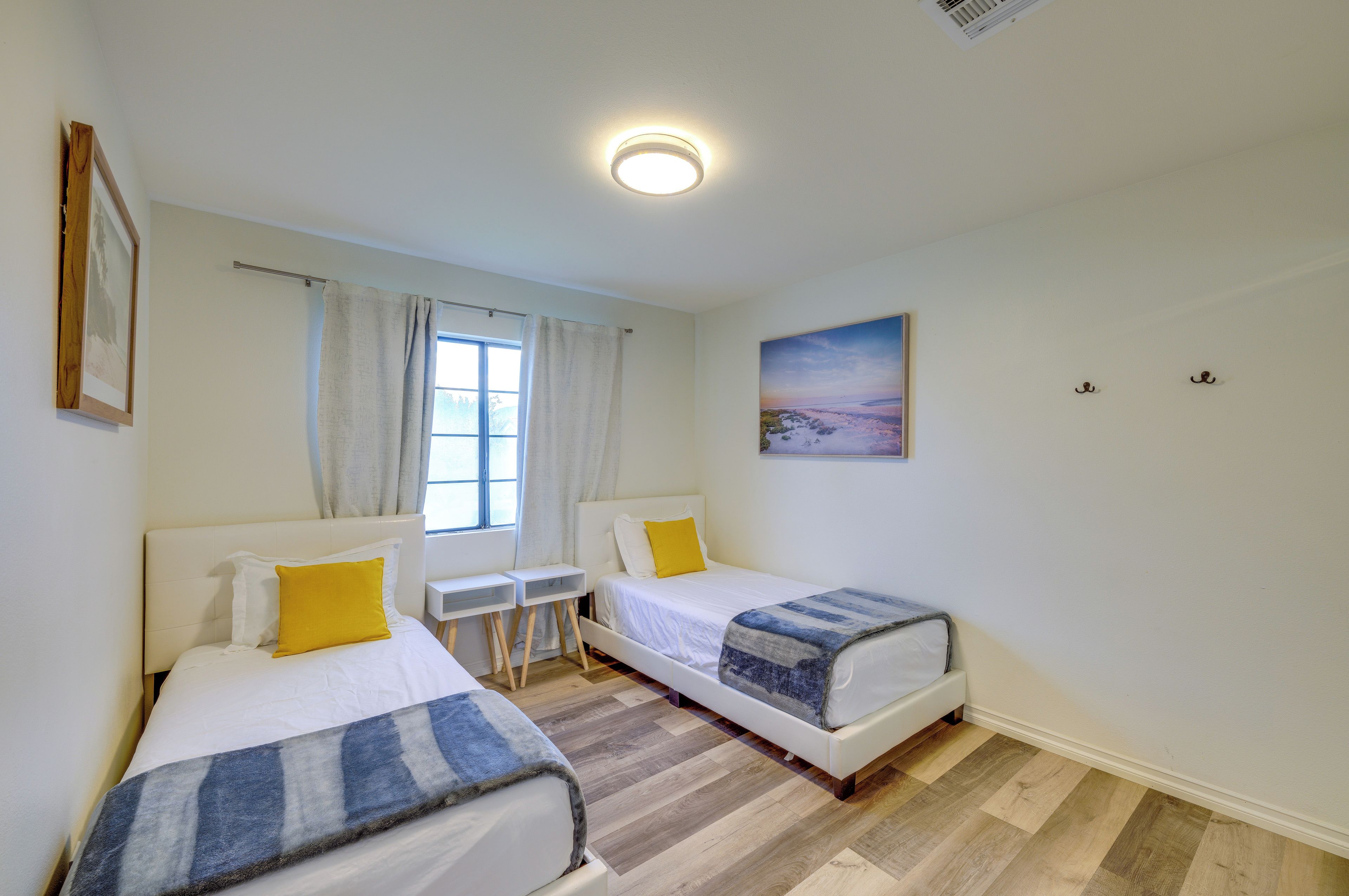Una habitación con dos camas, una ventana, un cuadro y una lámpara en el techo.