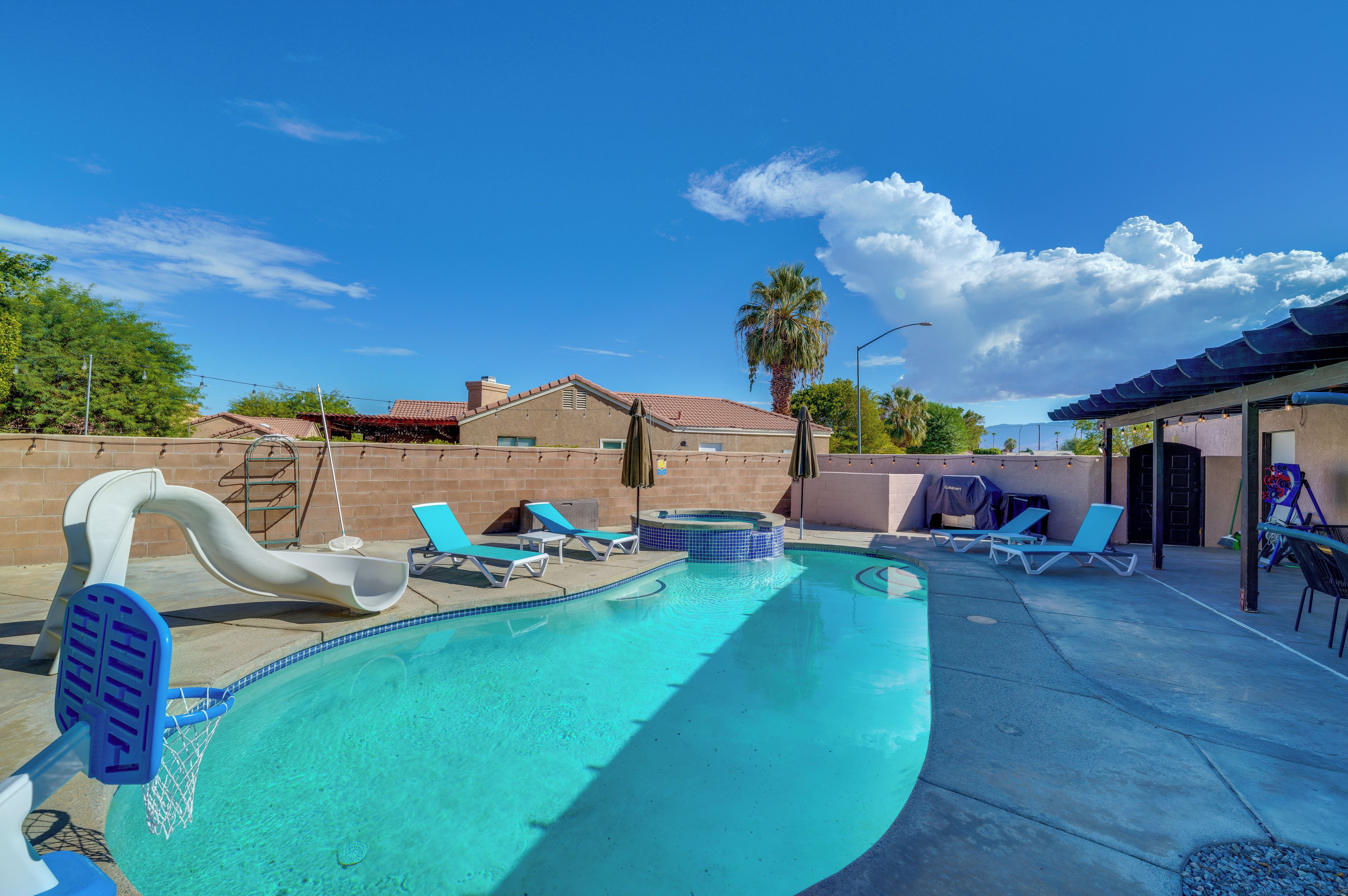 A swimming pool with a slide, lounge chairs, and a hot tub.
