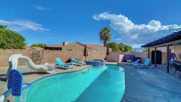 A swimming pool with a slide, lounge chairs, and a hot tub.