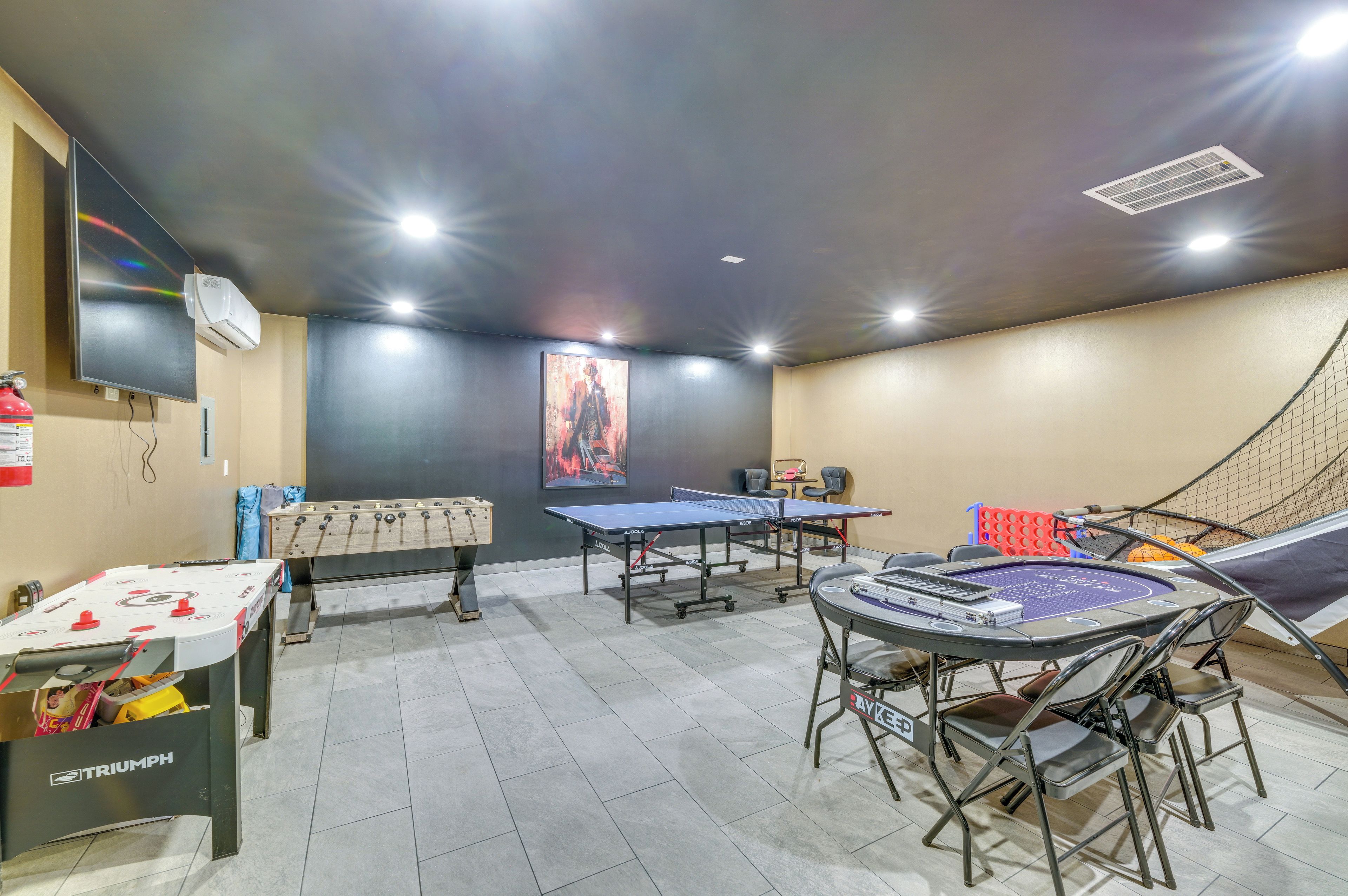 Una habitación con mesa de fútbol de mesa, mesa de ping pong y otra mesa de fútbol de mesa con mantel de marca.