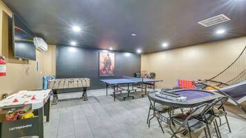 Una habitación con mesa de fútbol de mesa, mesa de ping pong y otra mesa de fútbol de mesa con mantel de marca.