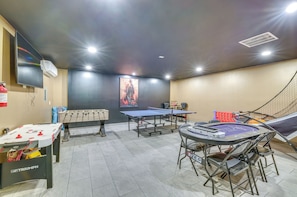 A room with a foosball table, ping pong table, and a foosball table with a branded tablecloth.