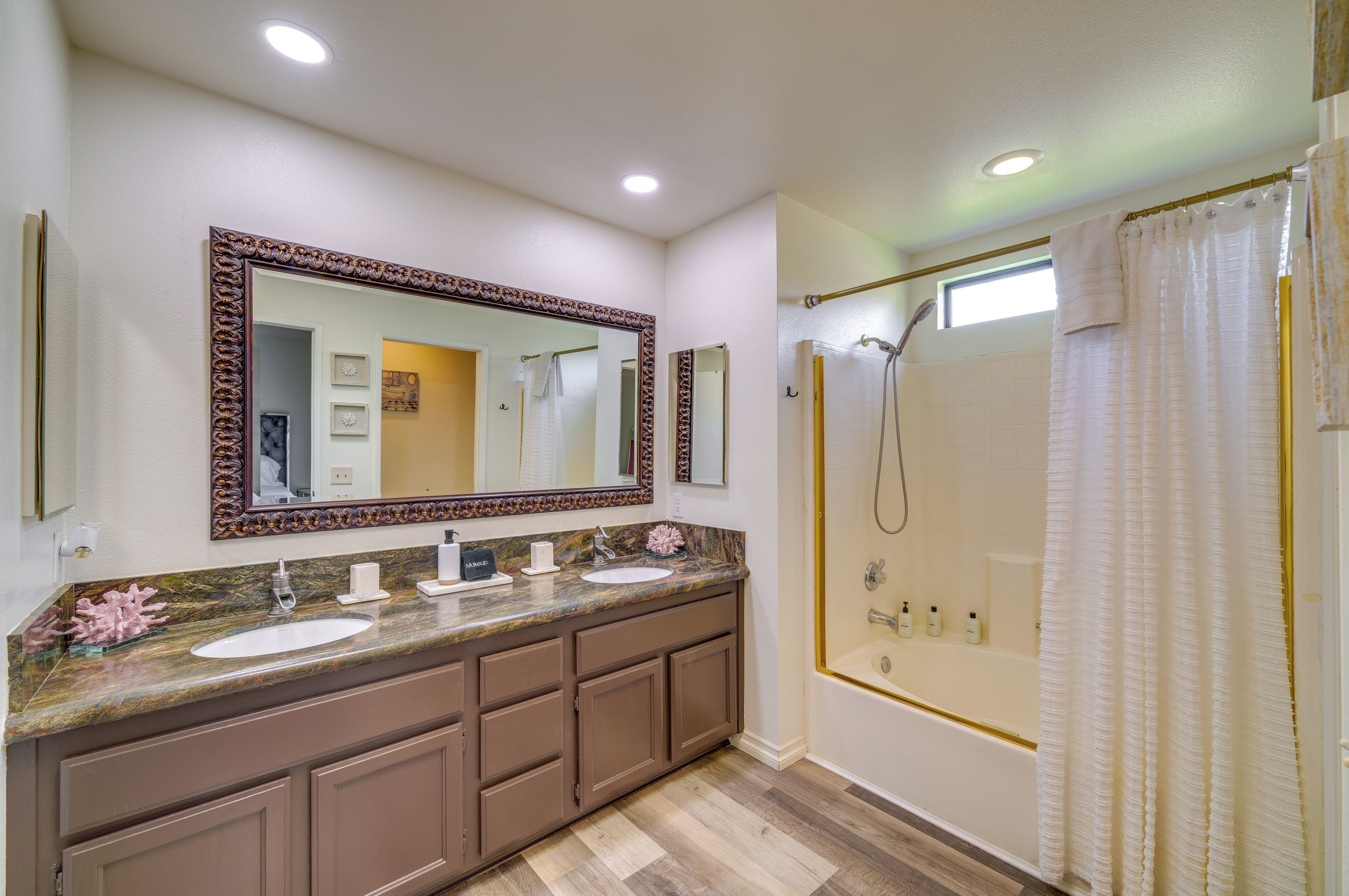 A bathroom with a double sink vanity, a large mirror, a shower with a glass door, and a window above the shower.