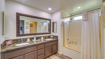 A bathroom with a double sink vanity, a large mirror, a shower with a glass door, and a window above the shower.