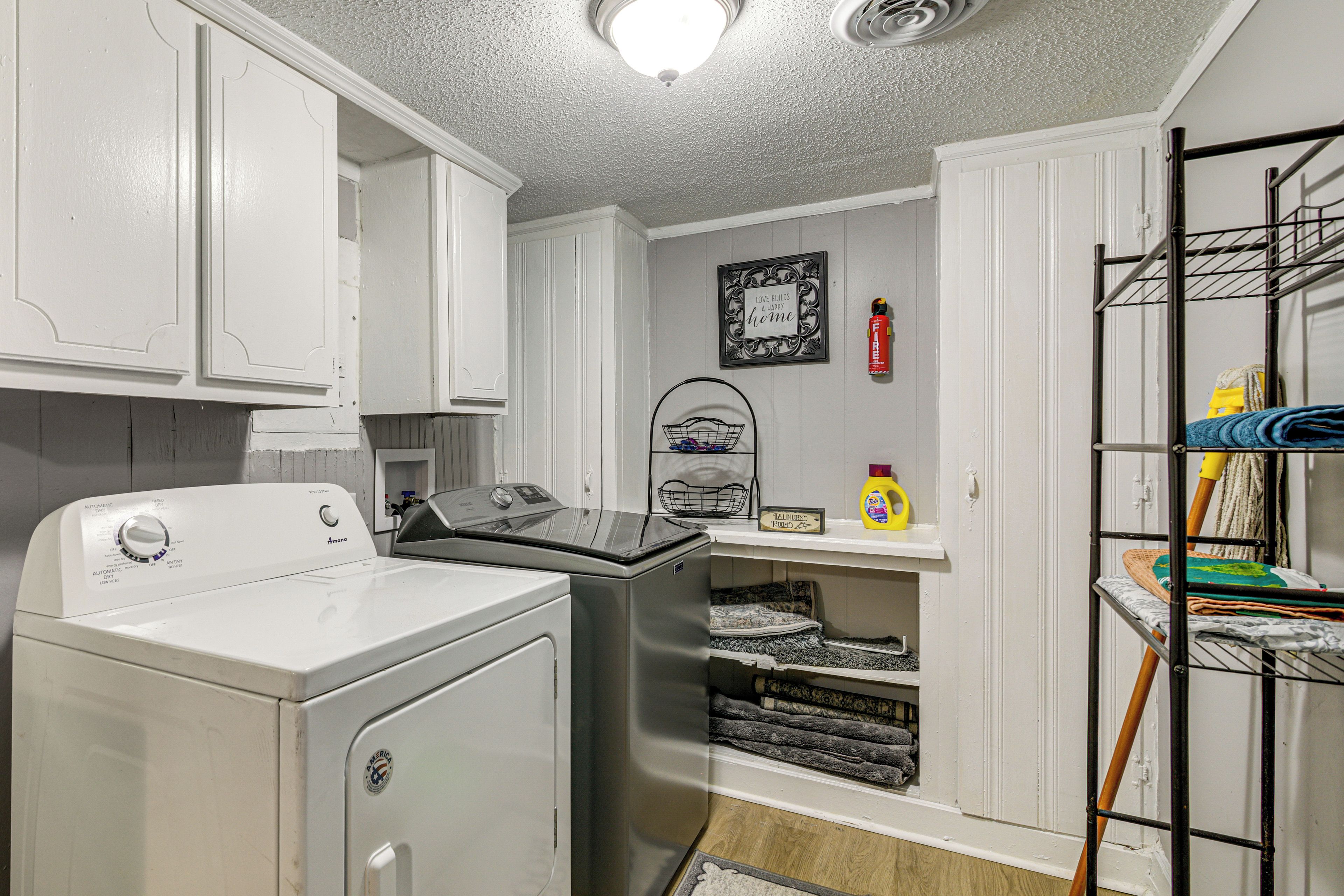 A compact laundry room with a front-loading washer and dryer, a small shelf with cleaning supplies, and a metal drying rack.
