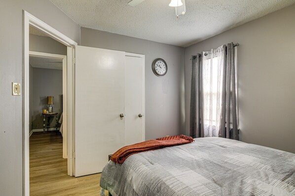 A bedroom with a bed, a door, a wall clock, and a window with curtains.