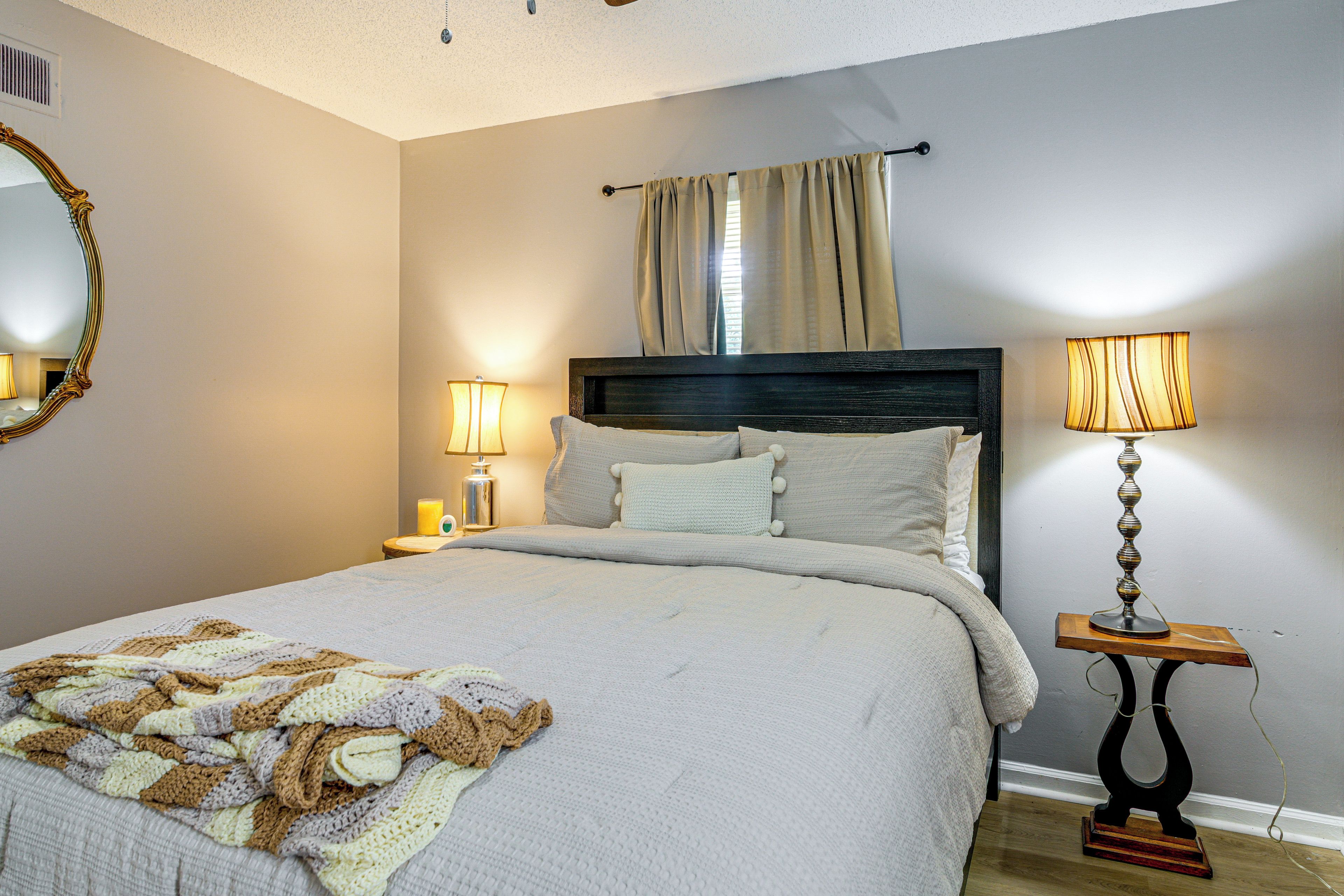 A neatly made bed with a knitted blanket, two bedside lamps, and a mirror on the wall.
