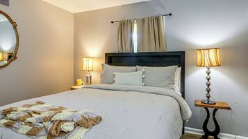 A neatly made bed with a knitted blanket, two bedside lamps, and a mirror on the wall.