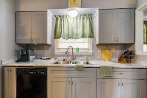 A kitchen with a built-in dishwasher, a coffee machine, a sink with a faucet, and a window with a green curtain.