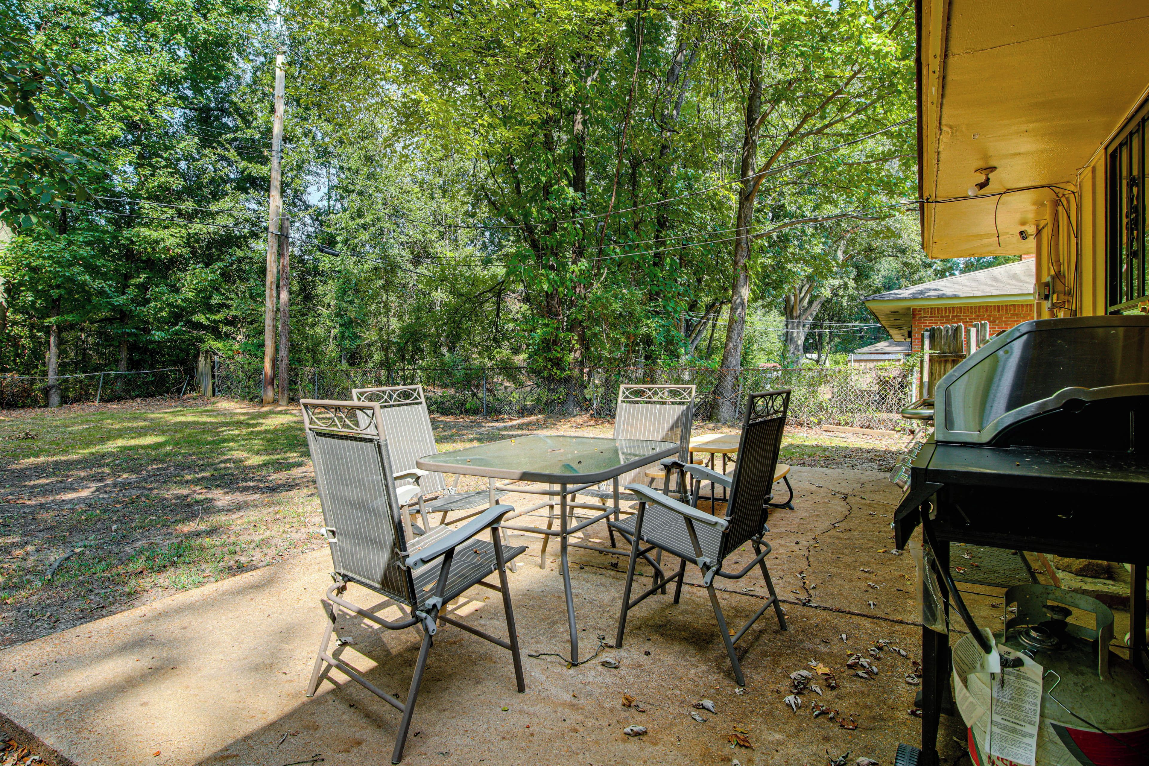 An outdoor patio with a table and chairs, surrounded by trees.